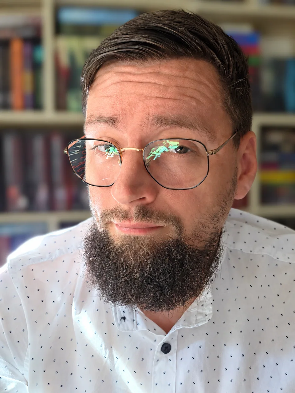 Paweł Piwowar in front of softly blurred bookshelves.